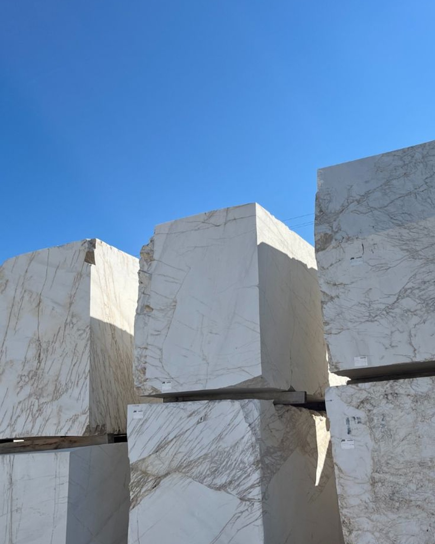 Raw blocks of marble stacked in a yard beneath a clear blue sky.