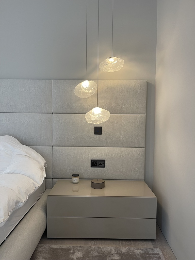 Bedside composition of sculpted glass pendants against the calm linen headboard wall