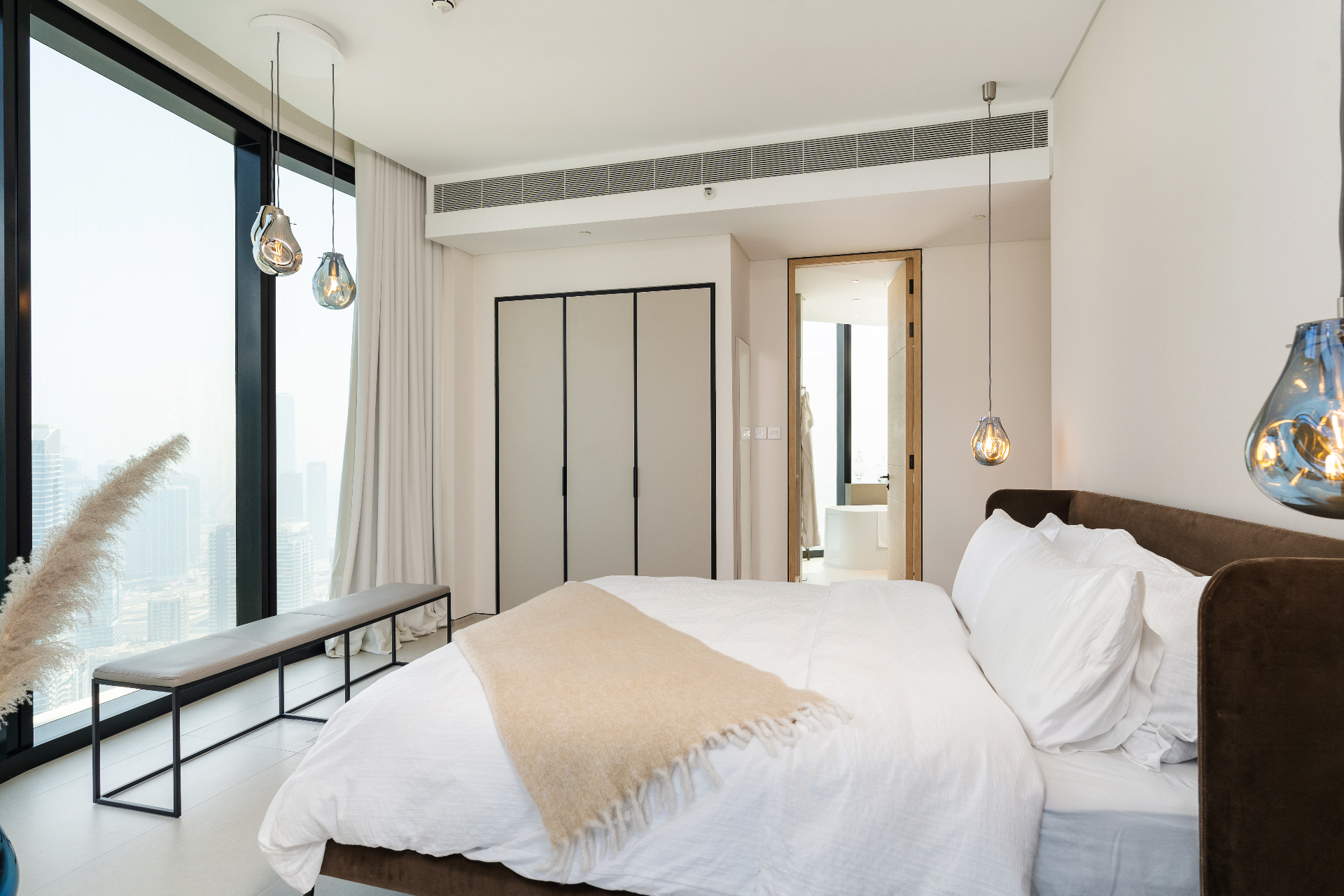 Primary bedroom with brown velvet headboard, linen bedding and blown-glass pendant lights against the skyline