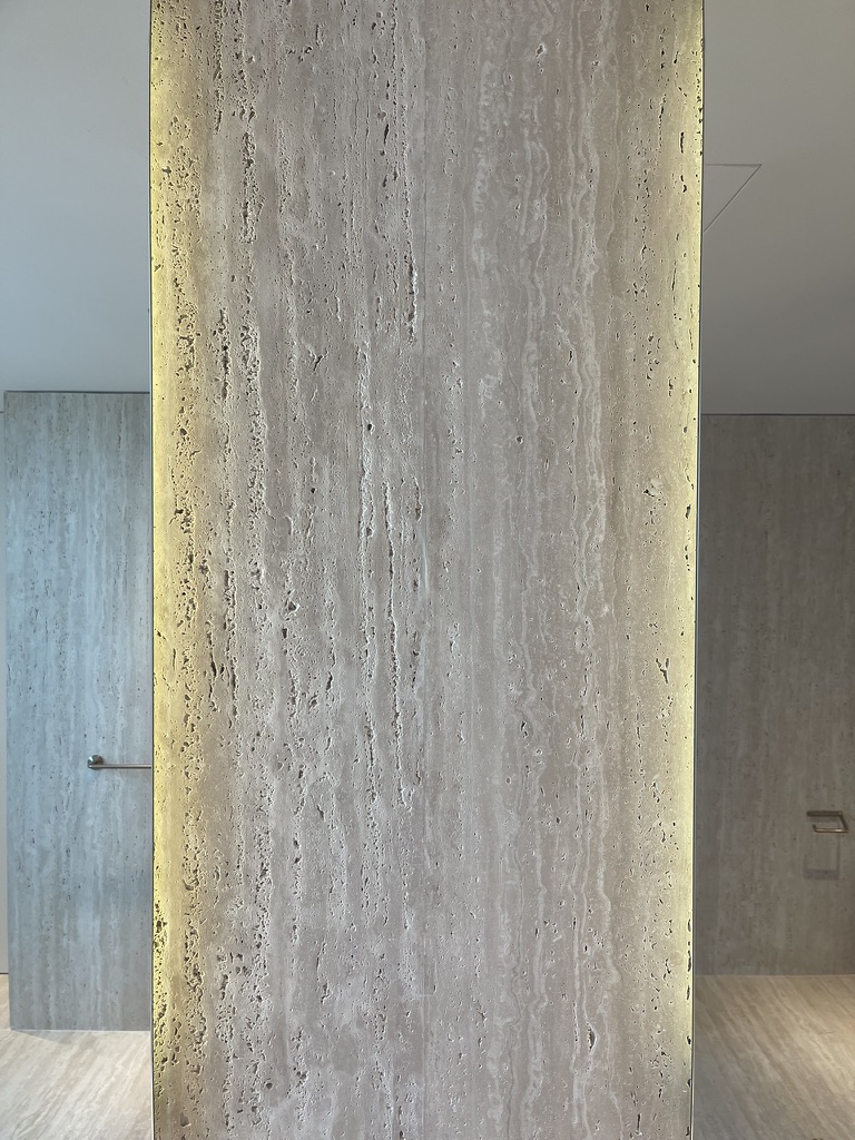 Backlit vein-cut travertine slab held between pale plaster walls as a singular material gesture