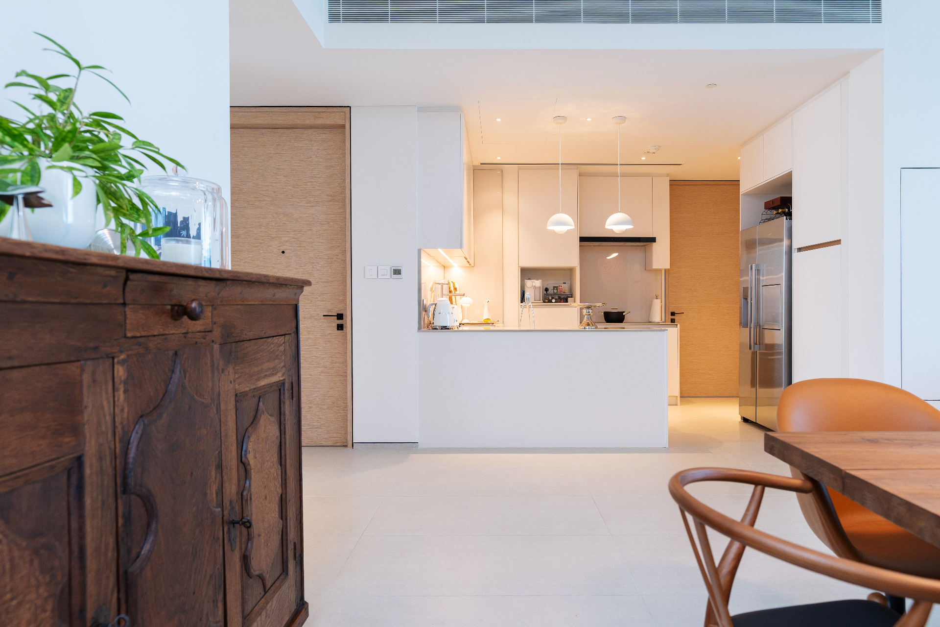 Kitchen with antique carved sideboard in the foreground, white lacquer cabinetry and dome pendant lights