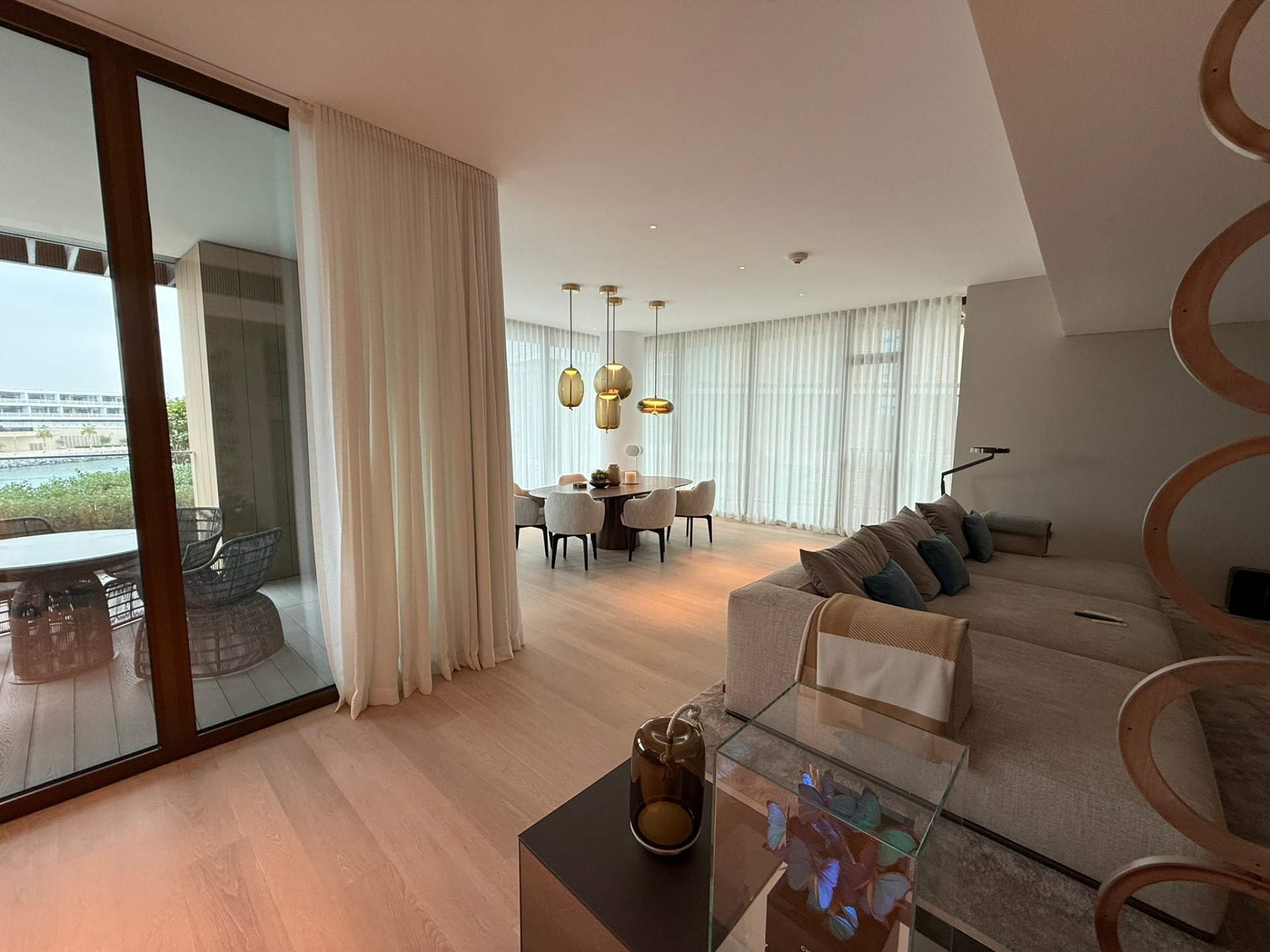 Living room opening toward the water with sheer drapery, low seating and a continuous horizon of glazing
