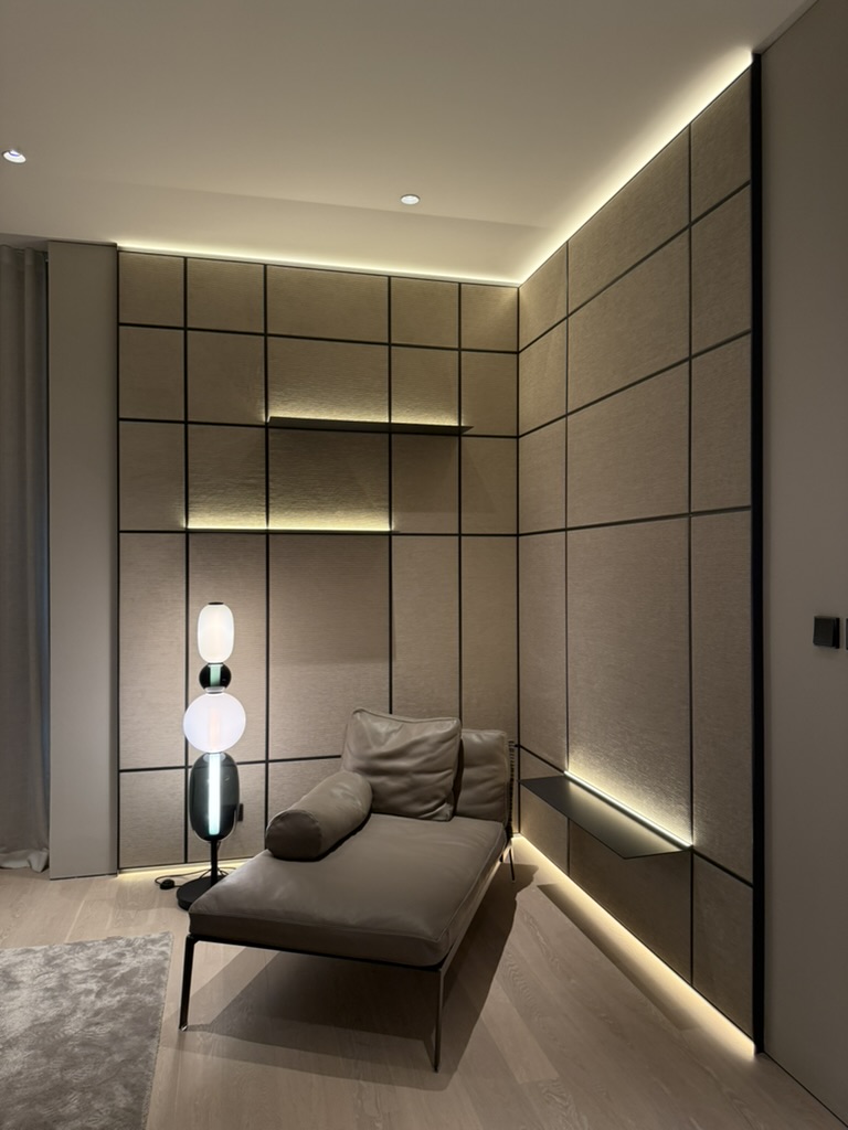 Quiet reading alcove lined in gridded leather panelling with a sculpted floor lamp and a low daybed washed in cove light