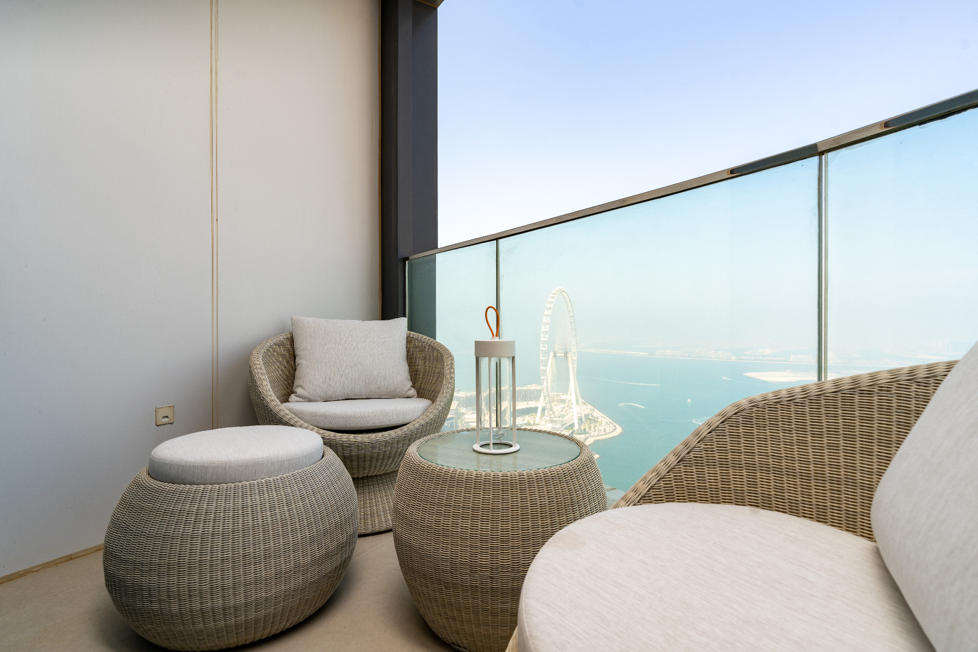 Balcony lounge at dusk — woven rattan armchairs and lantern overlooking the sea and Ain Dubai
