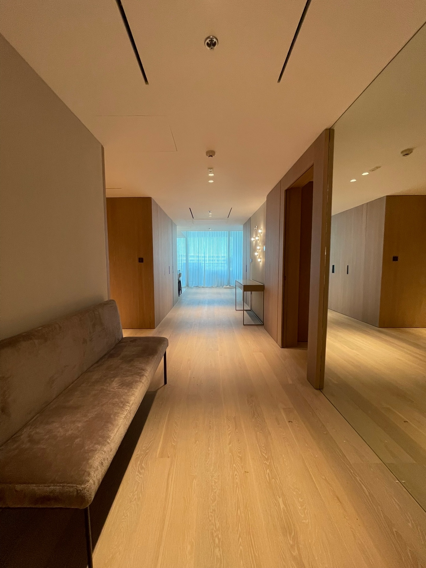 Hallway perspective lined in oak with a long bench, mirror and a calibrated pull of daylight at the end