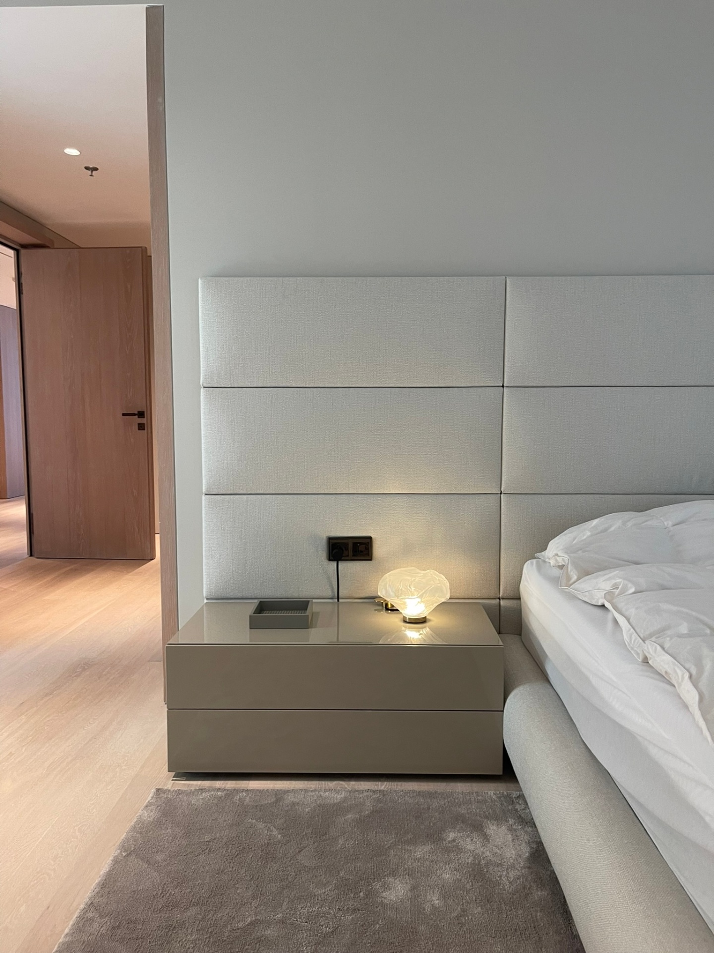 Primary bedroom in daylight with a restrained upholstered bed, pendant feature light and expansive corner glazing