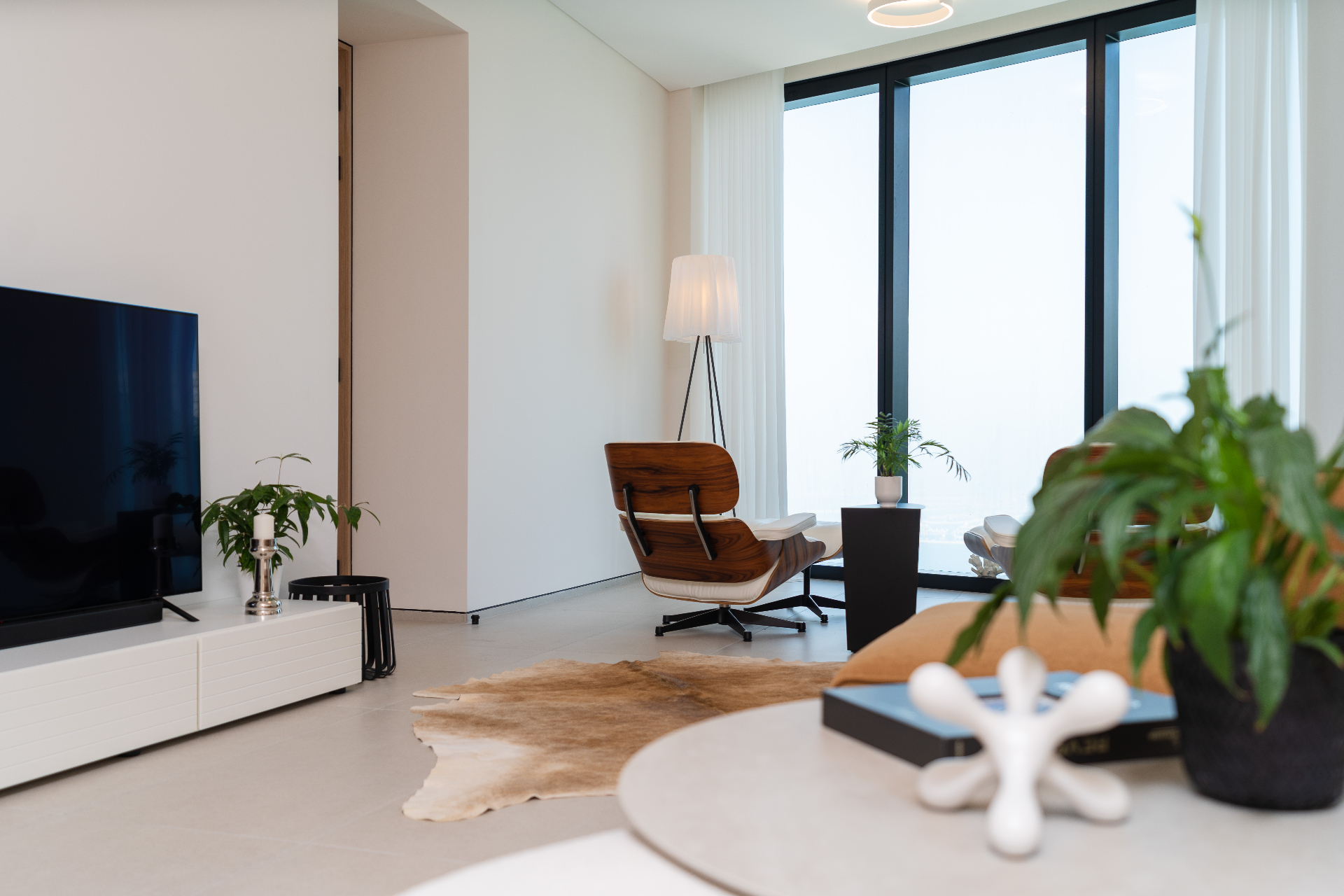Living room reading corner with rosewood lounge chair, tripod floor lamp and full-height windows