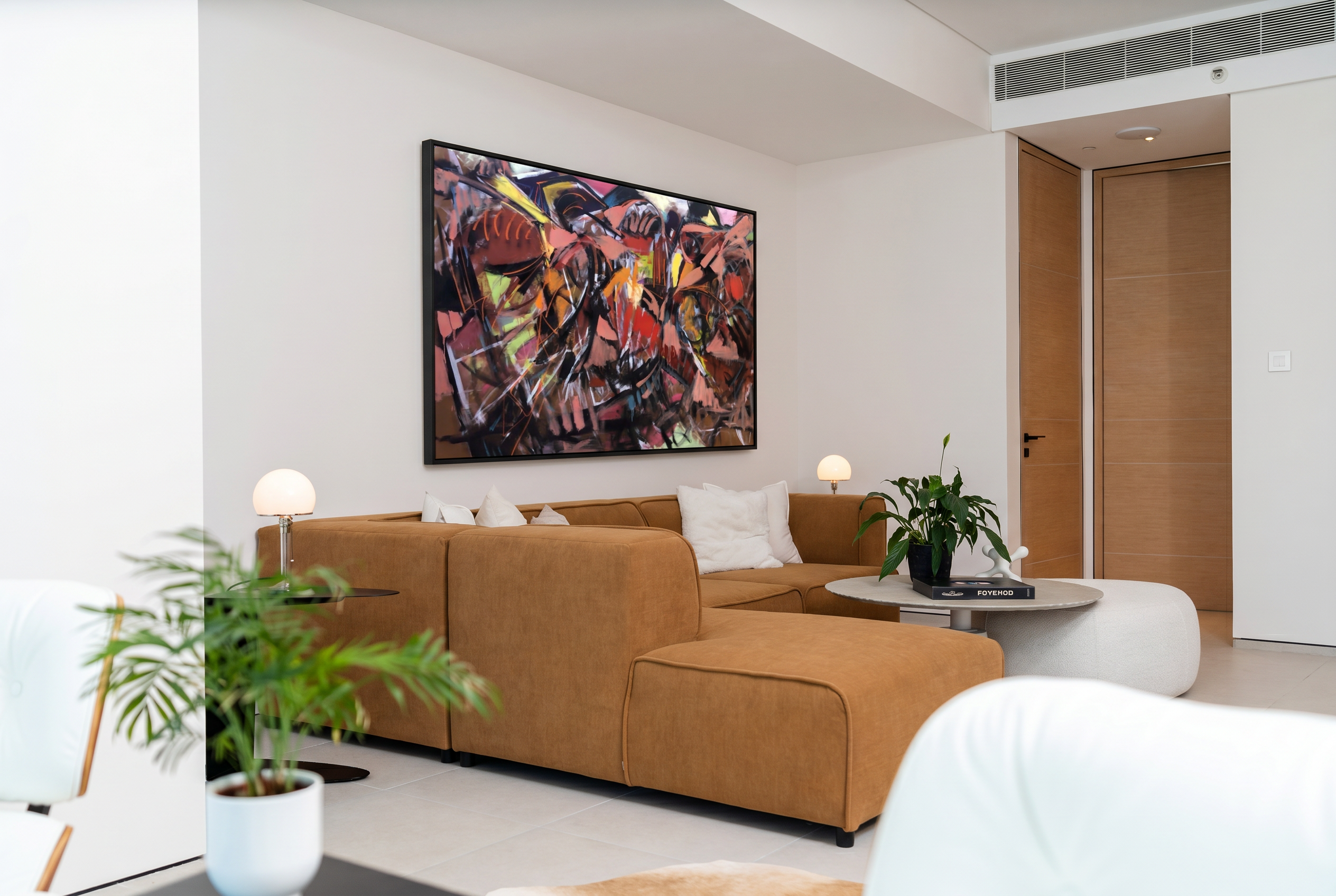 Living room with modular tan sectional, mushroom table lamps and framed artwork against warm white walls