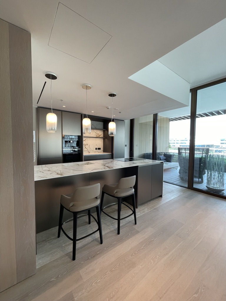 Kitchen with pale stone island, integrated cabinetry and full-height glazing beyond