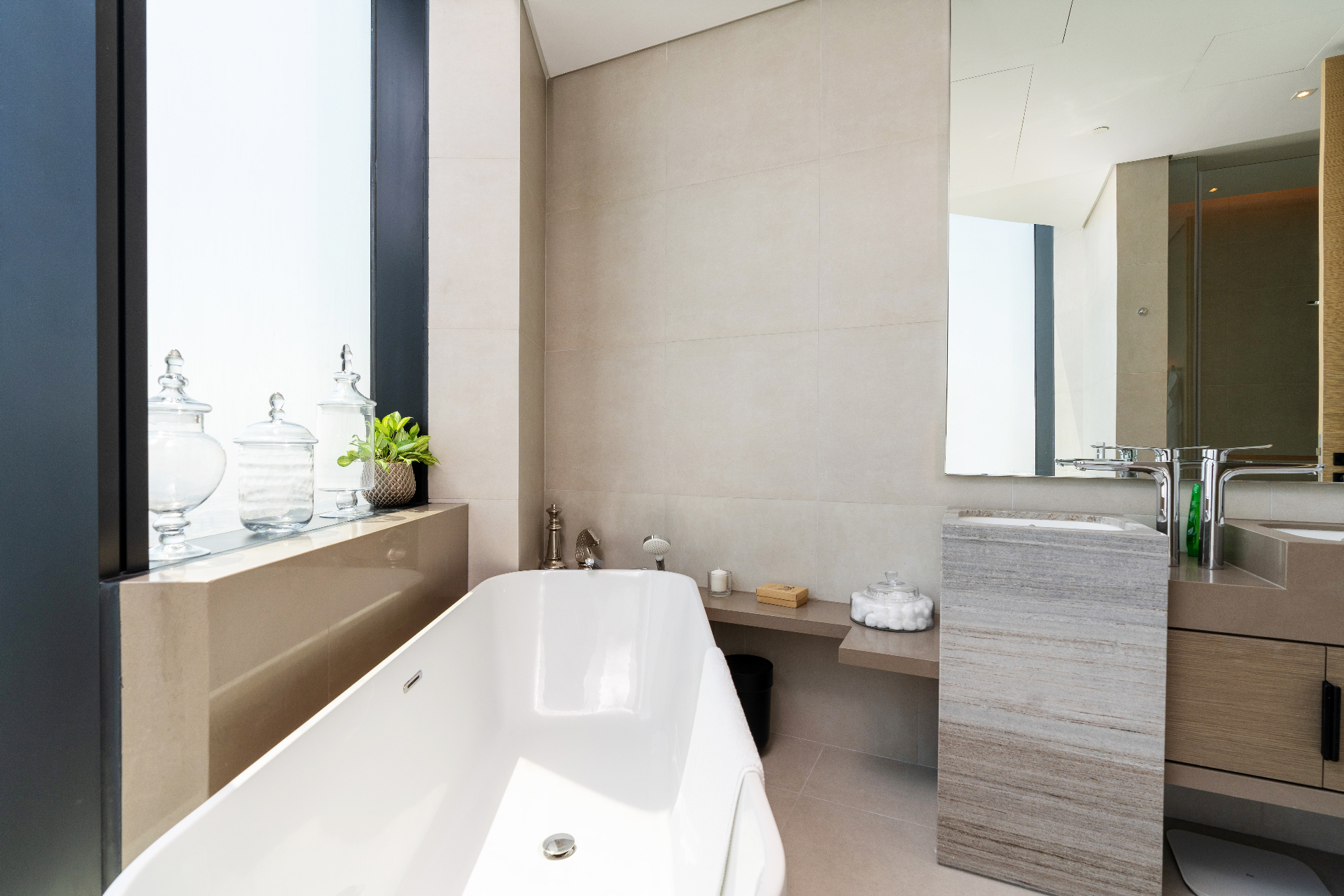Primary bathroom with freestanding soaking tub beside a full-height window, large-format stone tiles and travertine pedestal basin